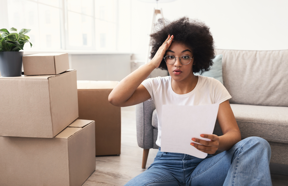 Woman holding her head with packing boxes around her.